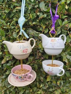 three tea cups and saucers with spoons in them hanging from the top of a tree