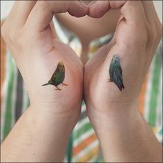 two small birds on the hands of someone with matching tattoos in front of their faces