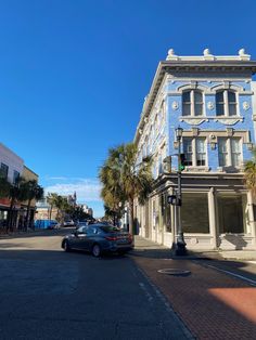 a car is parked on the street in front of a blue building with palm trees