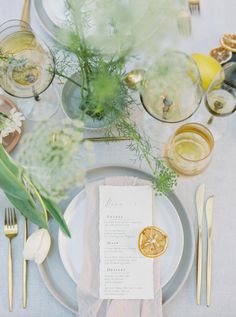 the table is set with white and gold plates, silverware, and greenery