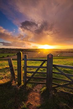 the sun is setting over an open field with a wooden fence in front of it