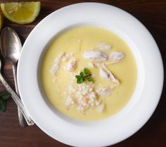 a white bowl filled with soup next to a spoon and lemon wedges on a wooden table