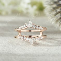 two rose gold wedding rings with diamonds on the top and bottom, sitting next to a pine cone