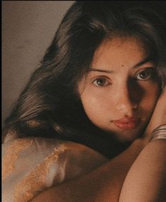 a beautiful young woman laying on top of a bed next to a wall with her hand on her head