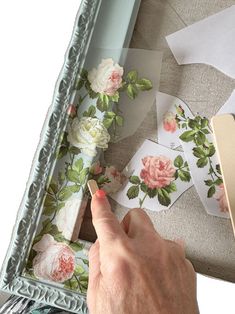 a hand is pointing at some flowers on a table with papers and scissors in front of it