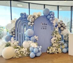 a blue and white backdrop with balloons, flowers and an arch that says it's my one