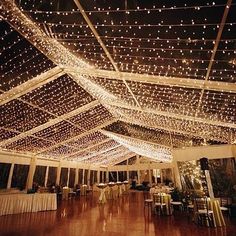 the inside of a tent with lights strung from it's ceiling and tables set up for an event