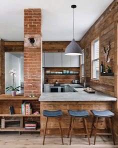 an open kitchen with brick walls and wooden flooring, along with two stools in front of the bar