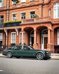 a green rolls royce parked in front of a large brick building with balconies