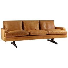 a tan leather couch with four pillows on it's back legs and arms, viewed from the front