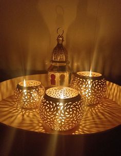 three lit candles sitting on top of a table next to a small candle holder with a lantern in the middle