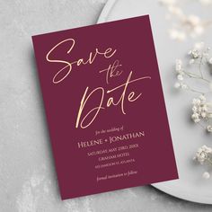 the burgundy and gold foil save the date card is next to some baby's breath flowers