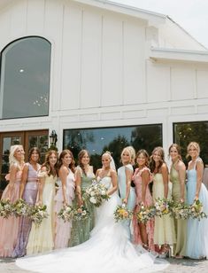 a group of women standing next to each other in front of a white building holding bouquets