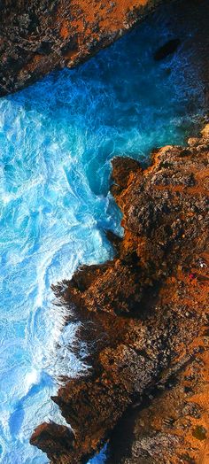 the water is blue and foamy next to some brown rocks with green moss growing on them