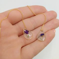 a hand holding two necklaces with purple flowers in them and one is hanging from a gold chain