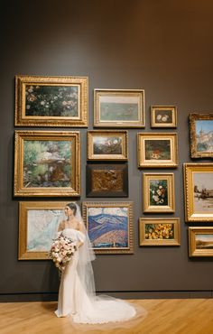 a bride standing in front of a wall with many framed pictures and paintings on it