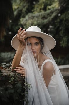 a woman wearing a white hat and veil is posing for a photo in the woods