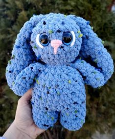 a blue crocheted stuffed animal with big eyes and nose is held up by someone's hand