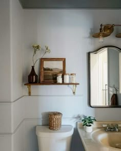 a white toilet sitting next to a sink in a bathroom under a mirror and a wooden shelf