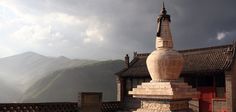 a statue on top of a building with mountains in the back ground and clouds in the sky