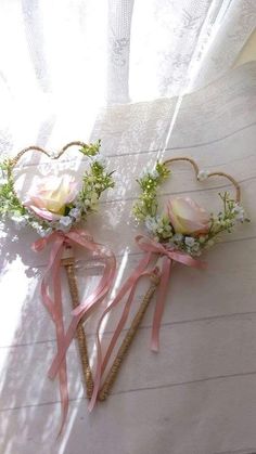 two heart shaped hair pins with flowers and ribbons attached to them on a white surface