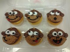 six cupcakes with chocolate frosting decorated to look like cartoon characters are in a plastic container