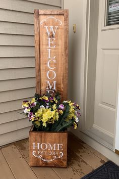 a wooden welcome sign sitting on top of a box filled with yellow and purple flowers