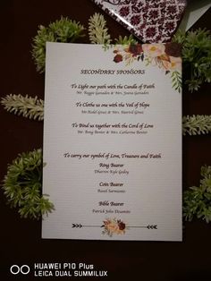 a wedding card with flowers and leaves on it, next to some greenery in the background