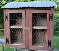 an old wooden cabinet with chicken wire on the top and bottom, sitting in front of a fence