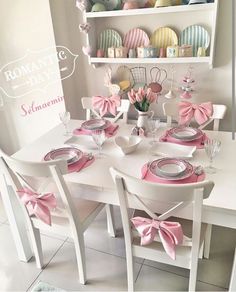 a white table topped with plates and pink bow ties next to a shelf filled with dishes