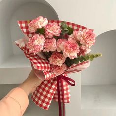 a hand holding a bouquet of pink carnations on a checkered table cloth