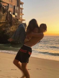 a man holding a woman on the beach at sunset