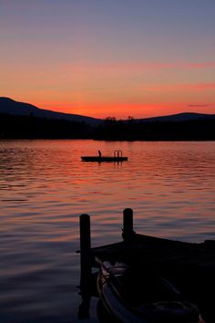 a boat floating on top of a lake next to a dock at sunset or dawn