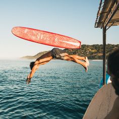 a man diving into the water from a boat with a surfboard in his hand