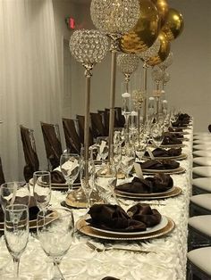 a long table is set with gold and silver plates, wine glasses, and balloons