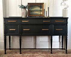 a black dresser with gold handles and drawers in front of a painting on the wall