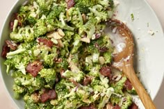 a bowl filled with broccoli and bacon on top of a table next to a wooden spoon