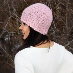 a woman wearing a pink crochet hat in front of some trees and branches