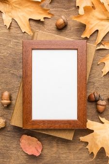 an empty wooden frame surrounded by leaves and acorns on a wood surface with space for text