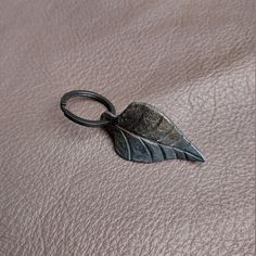 a leaf shaped metal object sitting on top of a brown leather surface with a ring around it