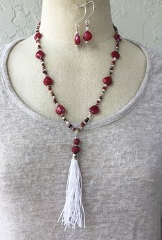 This handmade necklace and earrings set is made from a handmade white tassel with red dyed wood beads; semiprecious red jade faceted teardrops; glass seeds beads in brown, burgundy red, and white; and silver-tone components. Red Tassel Necklaces As Gifts, Red Tassel Necklaces For Gifts, Red Tassel Necklace For Gift, Red Round Beads Jewelry With Tassels, Red Tassel Jewelry With Round Beads, Adjustable Red Jewelry With Tassels, Adjustable Red Tasseled Jewelry, Red Jewelry With Tassels And Round Beads, Red Bohemian Teardrop Necklace