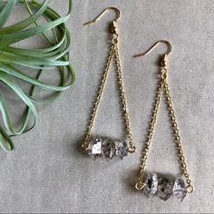 two pairs of gold tone earrings with clear crystal beads hanging from chain links on a gray surface