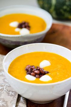 two white bowls filled with soup on top of a wooden table next to a pumpkin