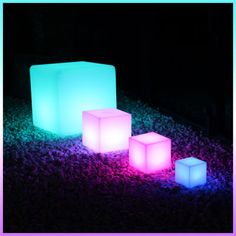 three illuminated cubes sitting on top of a bed of black grass at night time