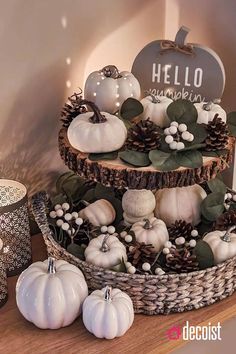 three tiered basket filled with white pumpkins and pineconis on top of a wooden table