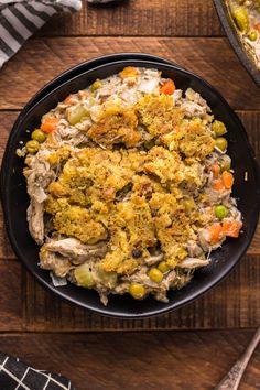 a black bowl filled with food on top of a wooden table next to silverware