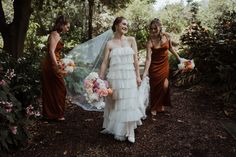 three bridesmaids are walking through the woods with their veil blowing in the wind