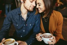 a man and woman sitting next to each other holding cups of coffee in their hands