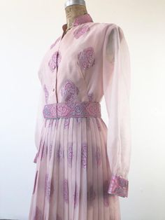 1960’s Alfred Shaheen pink oraganza maxi gown has an allover silver and pink foil print, with concentrated border motif at the hem and sleeve cuffs. There’s a matching printed removable belt that has hooks and grommets for closure. The dress has a sunburst pleated skirt, unlined sheer bishop sleeves, and a button front and cuffs. The dress body is lined in a pink rayon that becomes an underslip in the skirt. Made in USA. 91% polyester, 9% nylon.ConditionExcellent. Belt has wrinkling to vinyl and Festive Vintage Pink Dress, Pink Floor-length Maxi Dress With Pleated Bodice, Vintage Pleated Pink Skirt, Pink Vintage Dress With Button Closure, 1970s Pink Long Sleeve Dress, 1968 Pink & Orange Dress, Pink Foil, Body Dress, Maxi Gowns