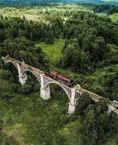 an aerial view of a train crossing a bridge in the middle of a green field